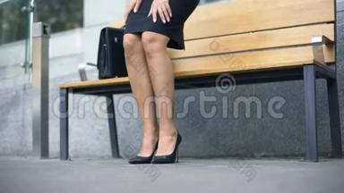 女人坐在长凳上，厌倦了穿着不舒服的<strong>高跟鞋走路</strong>